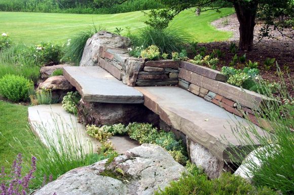 Каменная скамейка в саду природного дизайна